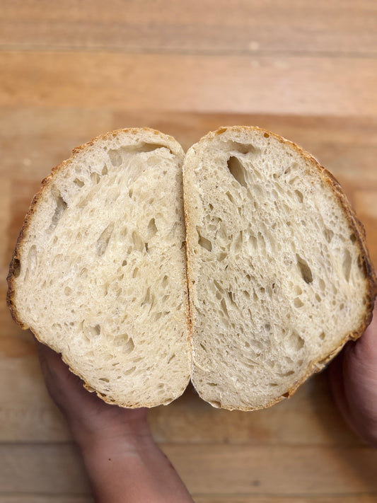 Half-cut sourdough bread held by a hand on a wooden surface