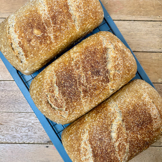 Three sourdough loaves of bread on a cooling rack with a wooden background