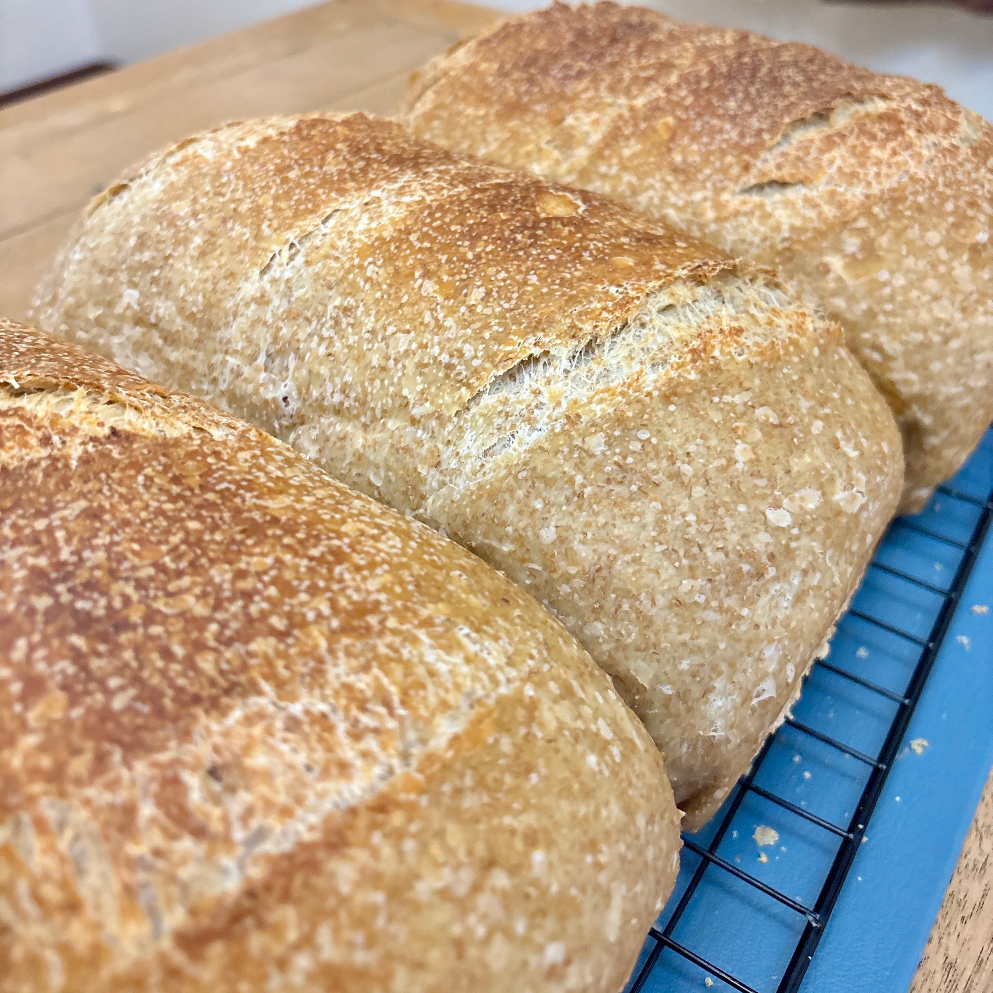 Three loaves of bread on a cooling rack with a wooden surface in the background
